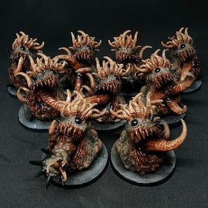 May include: A collection of eight miniature monster figurines, each featuring a textured brown and grey body, multiple tentacles, a wide mouth filled with sharp teeth, and a single dark eye, all mounted on individual circular black bases.