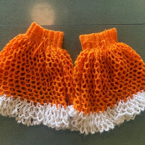 May include: Two crocheted orange skirts with white crocheted trim. The skirts are made with a mesh pattern.