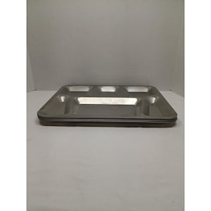 May include: A stack of stainless steel divided trays. Each tray has four compartments. The trays are rectangular with rounded corners and a shiny, metallic finish. The trays are stacked on top of each other.