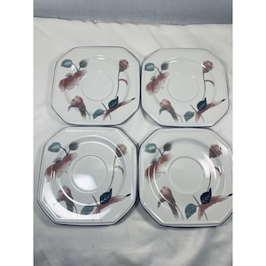May include: Set of four octagonal white saucers with a floral design. Each saucer features a central circular indentation and is decorated with pink and green floral motifs and a navy blue border.