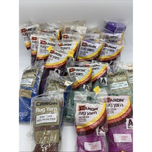 May include: A collection of Caron Rug Yarn in various colors, packaged in clear plastic. The labels read "Rug Yarn" and "Easy Care 100% Acrylic Fiber." Colors include purple, green, blue, and brown. Each package contains 320 pieces.