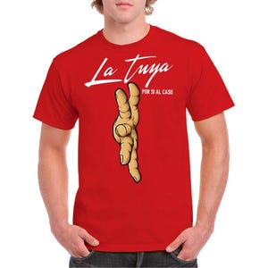 Könnte beinhalten: Rotes T-Shirt mit dem weißen Schriftzug "La Tuya" über einer Cartoon-Hand-Illustration. Der Satz "POR SI AL CASO" ist darunter in kleinerer Schrift gedruckt.