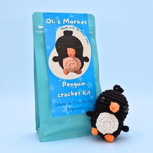 Puede incluir: Un kit de crochet para hacer un ping&uuml;ino, presentado en una bolsa azul y blanca. El kit incluye hilo, un gancho de crochet e instrucciones para hacer un ping&uuml;ino. La bolsa tiene el texto "Oli's Market Made with No Mess-yarn Penguin crochet Kit Learn to Crochet For Beginners" impreso en ella.
