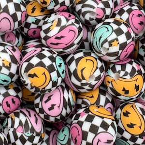 May include: A close-up of a group of colorful silicone beads with a checkered pattern and smiley face designs. The beads are perfect for making necklaces, bracelets, or other jewelry.