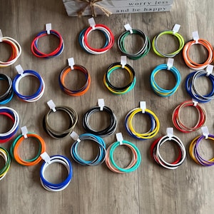 May include: A collection of numerous multi-colored silicone bracelets arranged in groups, each secured with a small white paper tag. The bracelets feature a variety of solid colors including red, blue, green, yellow, orange, black, white, and gray.