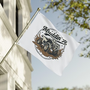 May include: White flag with the words "Muddin It" in a stylized font, featuring a graphic of an ATV splashing through mud. The design is in black, brown, and white, with a circular border and star accents.