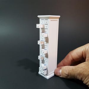 Könnte beinhalten: Ein weißer Miniatur-Schrank mit mehreren Schubladen, von denen einige geöffnet sind. Der Schrank ist etwa 25 cm hoch und aus Holz gefertigt.