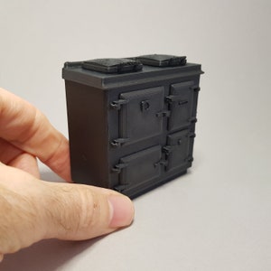 Pode incluir: Um fogão de ferro fundido em miniatura preto com duas portas de forno e dois queimadores superiores. O fogão é feito de plástico e tem cerca de 15 cm de altura.