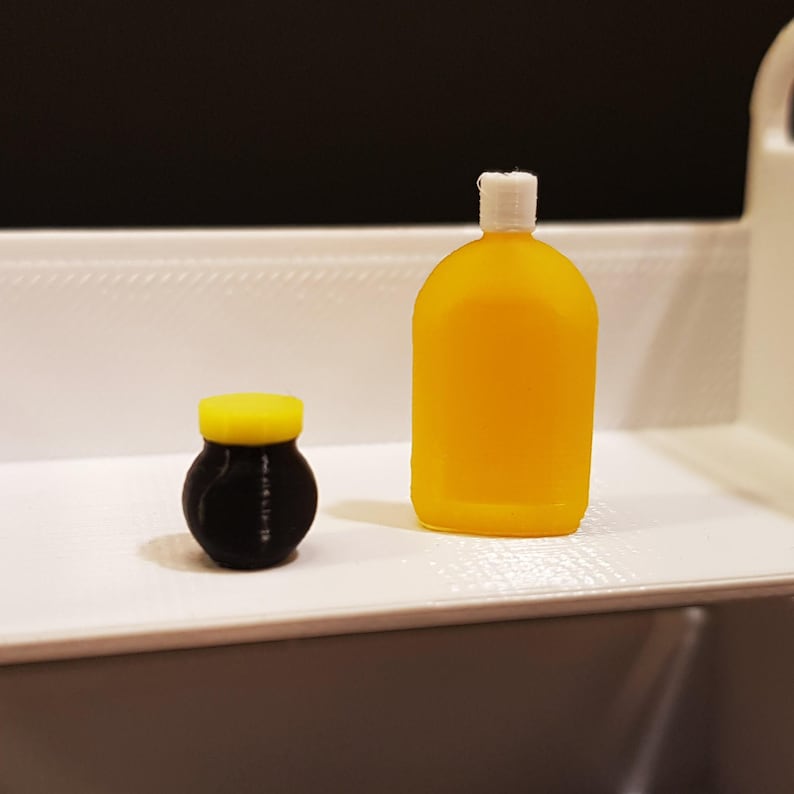 May include: A small yellow and black jar and a larger yellow bottle, both on a white shelf.