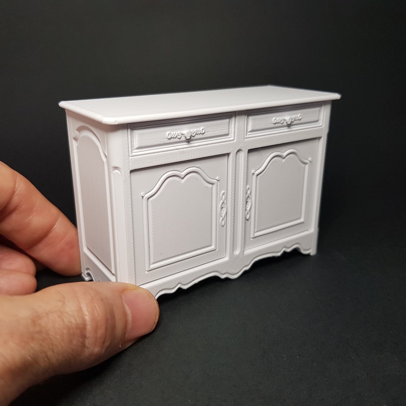 May include: White painted wooden cabinet with two doors and two drawers. The cabinet has ornate details and a slightly curved base.