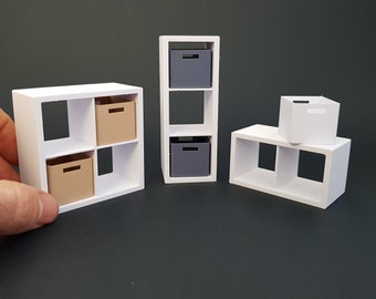 May include: Three white cube shelves with removable storage boxes. The shelves are made of white plastic and have a modern design. The boxes are beige and gray.
