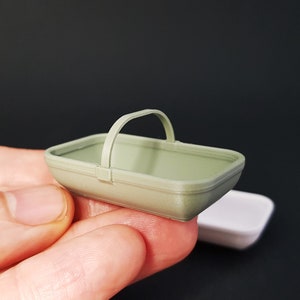 May include: A small, green plastic basket with a handle. The basket is empty and appears to be made for miniature or dollhouse use.