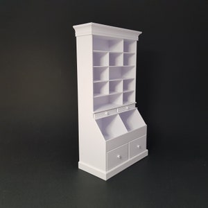 Può includere: Libreria in legno bianco con ripiani aperti e due cassetti. La libreria ha una cornice superiore decorativa e una base con due cassetti. La libreria è su uno sfondo nero.