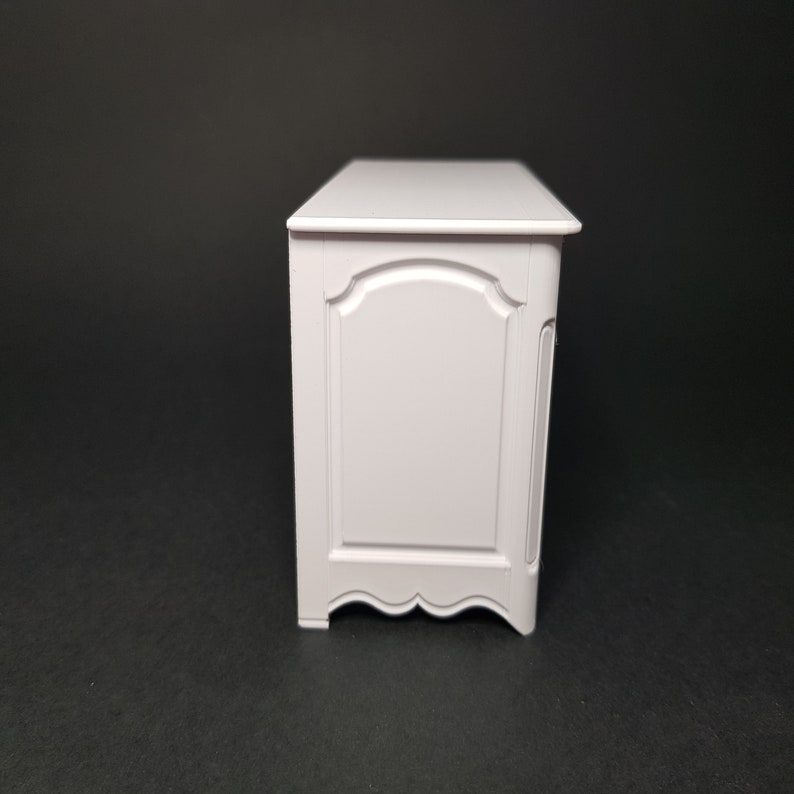 May include: White wooden dresser with a single drawer and ornate detailing. The dresser has a simple, elegant design.