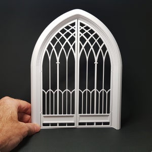 May include: White arched double door with a decorative, intricate, geometric, lattice design. The door is made of plastic and is approximately 12 inches tall.