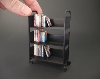 May include: A black metal bookshelf with three shelves, filled with a variety of books. The bookshelf is on wheels and has a black background.