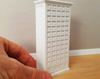 May include: White wooden cabinet with a large number of small drawers. The cabinet has a single drawer at the bottom.