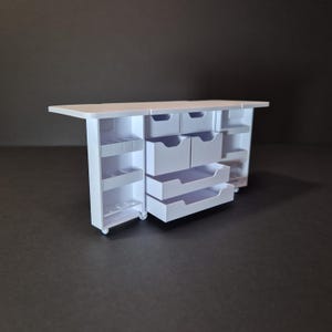 May include: A white miniature storage cabinet with multiple drawers and shelves. The cabinet has a rectangular top and is on wheels. The drawers are open, revealing the interior. The shelves are on the sides of the cabinet.
