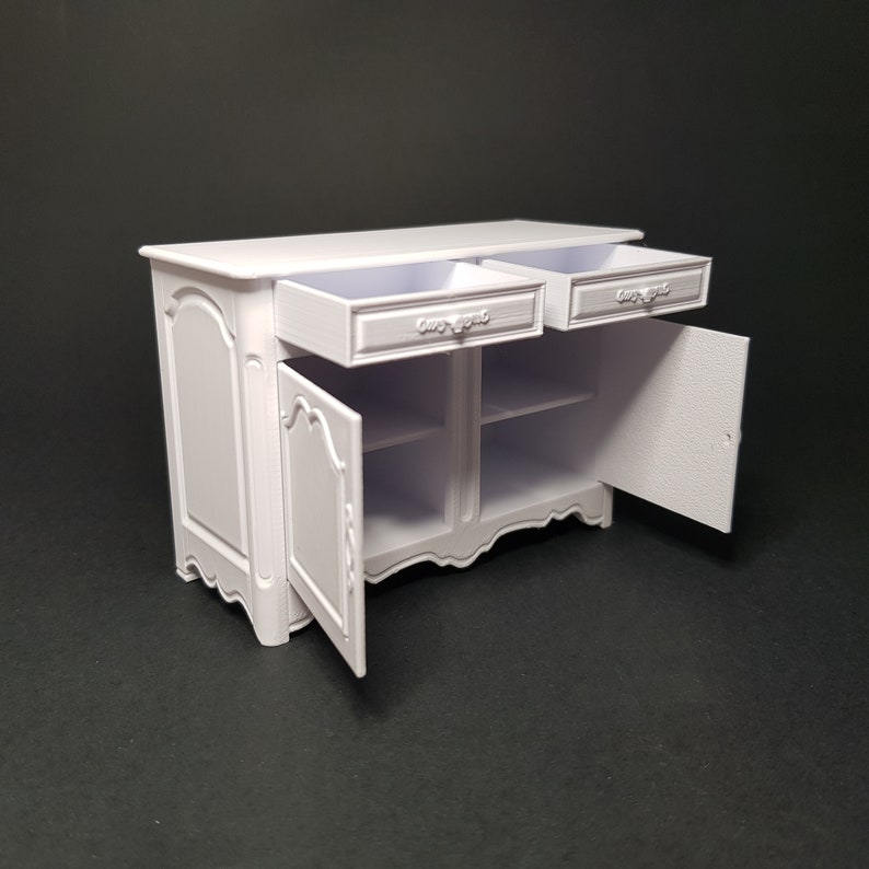 May include: White wooden cabinet with two drawers and two doors. The doors are open, revealing two shelves inside. The cabinet has a decorative design on the front.