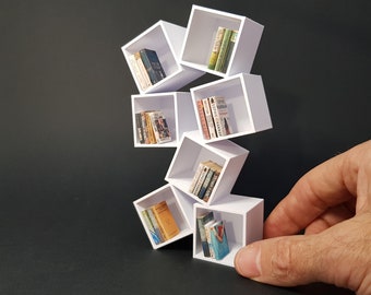 May include: White miniature bookshelf with multiple shelves stacked in a staggered formation. The shelves are filled with miniature books with colorful spines. The bookshelf is on a dark gray background.