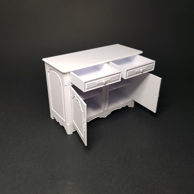 May include: White wooden cabinet with two drawers and two doors. The doors are open, revealing empty shelves inside. The cabinet has a decorative, ornate design.