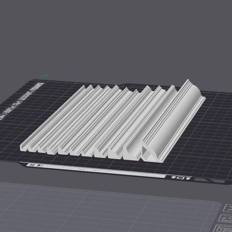 May include: A close-up of a set of 12 white plastic moldings, each with a slightly different shape and size. The moldings are arranged in a row on a black grid surface.