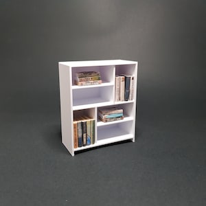 May include: White bookshelf with five shelves, filled with books. The books are organized by color and size. The bookshelf is made of wood and has a modern design.