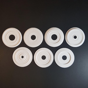 May include: Eight white ceiling medallion covers with different designs. The medallions are round and have a hole in the center.