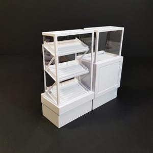 Puede incluir: Vitrina de exposición blanca con tres estantes y un frente de vidrio. La vitrina está hecha de plástico y tiene una base blanca. La vitrina está sobre un fondo negro.