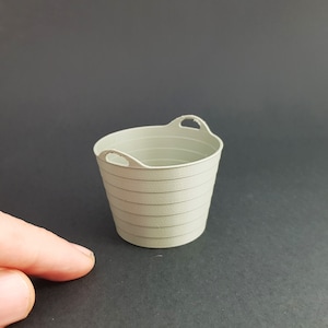 Puede incluir: Un pequeño cubo de plástico gris con dos asas. El cubo tiene una textura acanalada.