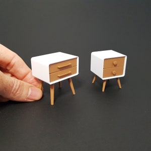May include: Two white bedside tables with brown drawers and wooden legs. The tables are on a black surface.