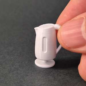 May include: A small white plastic pitcher with a handle and a round base. The pitcher is about the size of a person's thumb.