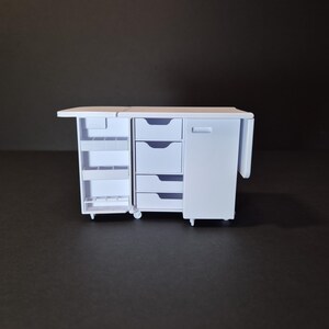 May include: A white miniature cabinet with multiple storage options. It features a pull-out shelf, three drawers, a cabinet door, and a side extension. The cabinet is on wheels and has a clean, minimalist design.