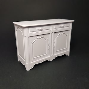 Puede incluir: Un aparador de madera pintado de blanco con dos cajones y dos puertas. El aparador tiene tallas ornamentadas y una base curva.