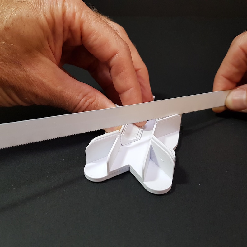 May include: A white paper craft project being cut with a serrated blade. The project is shaped like a star with multiple points and has a series of cutouts.