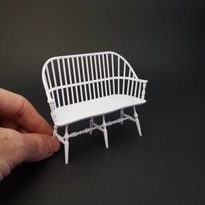 May include: White wooden bench with a slatted back and curved arms. The bench has a simple design with turned legs and spindles.