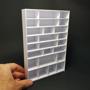 May include: White, freestanding, multi-tiered shelf unit with 18 individual compartments. The shelf unit is made of a sturdy material and is ideal for organizing and displaying small items.