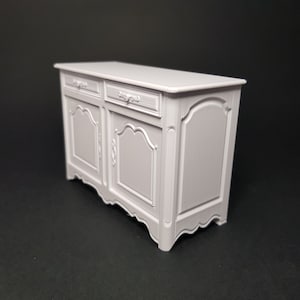 May include: A white painted wooden sideboard with two drawers and two doors. The doors have ornate carvings and the drawers have simple metal handles.