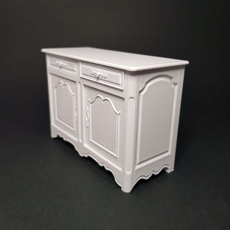 May include: A white painted wooden sideboard with two drawers and two doors. The doors have ornate carvings and the drawers have simple metal handles.