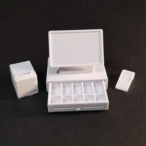 May include: White cash register with a monitor, a drawer with compartments, and a separate white card reader.