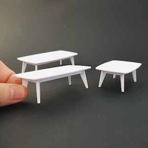 以下が含まれることがあります： 3つの異なるサイズの白いコーヒーテーブル。一番大きなテーブルは背景にあり、中くらいのテーブルは前景にあり、一番小さなテーブルは右隅にあります。
