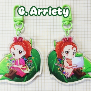 May include: Two keychains featuring a cartoon girl with red hair, sitting on a green leaf with flowers. The keychains have a green clasp and the text "G. Arrietty" in green.