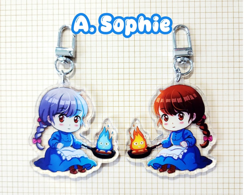 May include: Two acrylic keychains featuring anime-style illustrations of a character in a blue dress, holding a pan with a flame. One keychain has a character with purple hair, the other with red hair. The text "A. Sophie" is above.