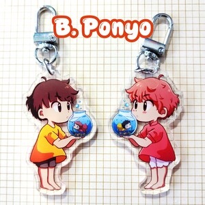 May include: Two clear acrylic keychains featuring anime-style characters holding fishbowls. One character wears a yellow outfit, the other a red outfit. Each keychain has a silver-colored clasp. The text "B. Ponyo" is at the top.