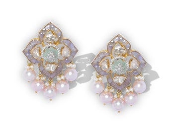 Puede incluir: Un par de pendientes dorados ornamentados. Cada pendiente presenta un diseño floral con una piedra verde claro central rodeada de diamantes. Los pendientes tienen un borde lavanda y blanco y están adornados con perlas rosas colgantes.