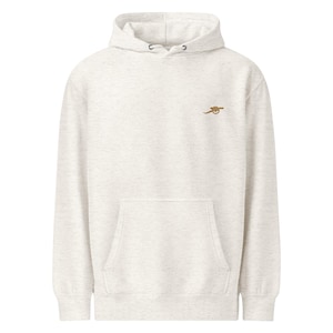 May include: A light grey hoodie with a kangaroo pocket and a drawstring hood. The hoodie features a small, embroidered gold cannon logo on the upper left chest. The fabric has a speckled texture.