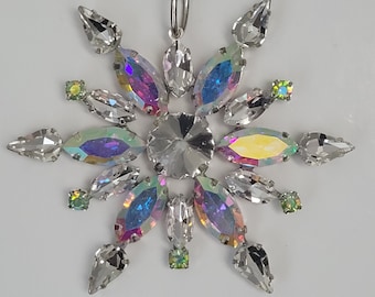 May include: A silver snowflake ornament with iridescent crystals and green accents. The snowflake is hanging from a silver ribbon.