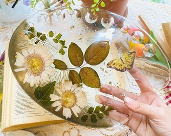 May include: A clear resin artist's palette with pressed flowers, leaves, and a butterfly. The palette has a textured surface with small, clear circles.