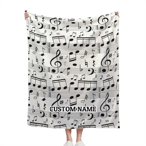May include: White fleece blanket with a black and white musical note pattern. The blanket has the text "CUSTOM NAME" printed on it.