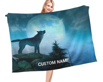 Puede incluir: Una manta de forro polar azul con un lobo aullando a la luna. La luna está llena y brillante, y el lobo está silueteado contra ella. La manta tiene un fondo azul oscuro con nubes blancas. El texto "CUSTOM NAME" está impreso en la manta.